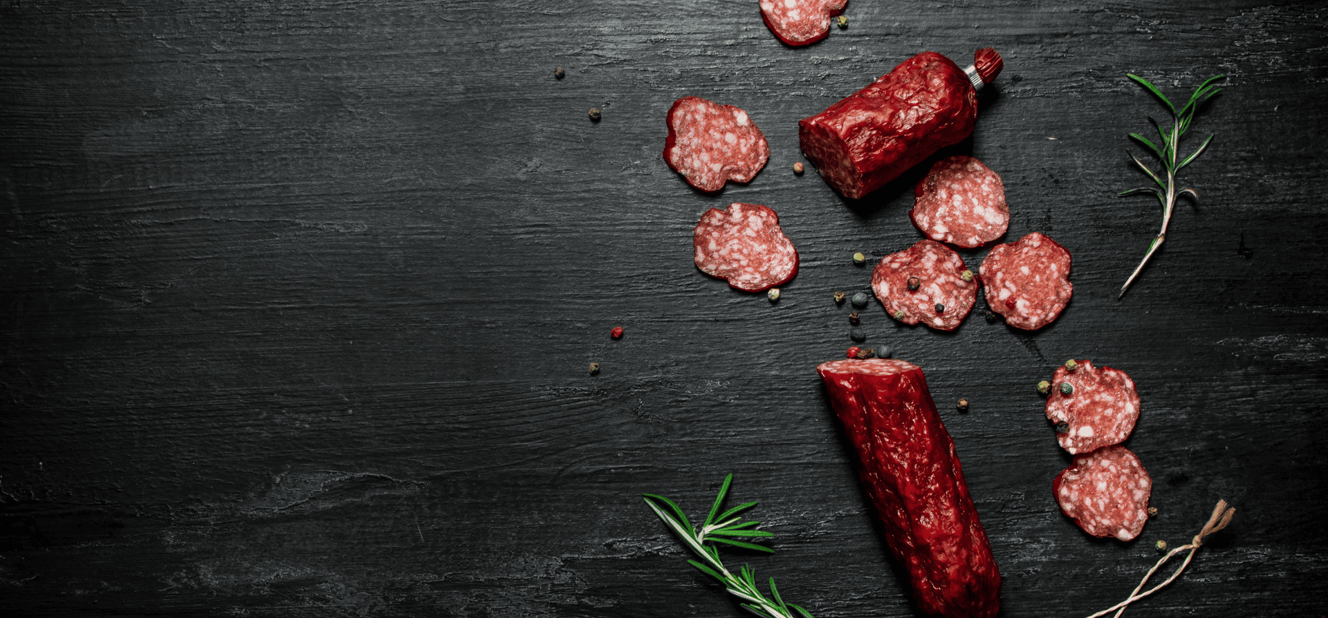 Auf schwarzem Hintergrund liegt in Scheiben geschnittene Salami mit Gewürzen